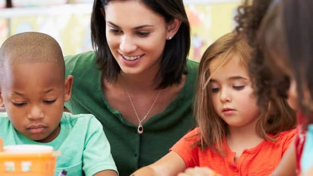 Children engaged in art activities with a smiling teacher, surrounded by colorful craft supplies.