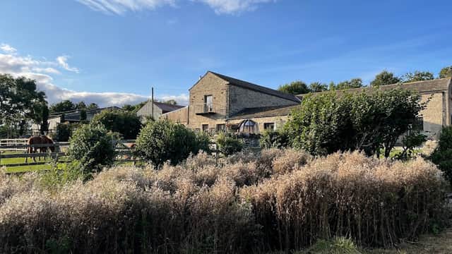 Craken House Farm features stone buildings, lush greenery, horses, and a clear blue sky in Harmby, Yorkshire.