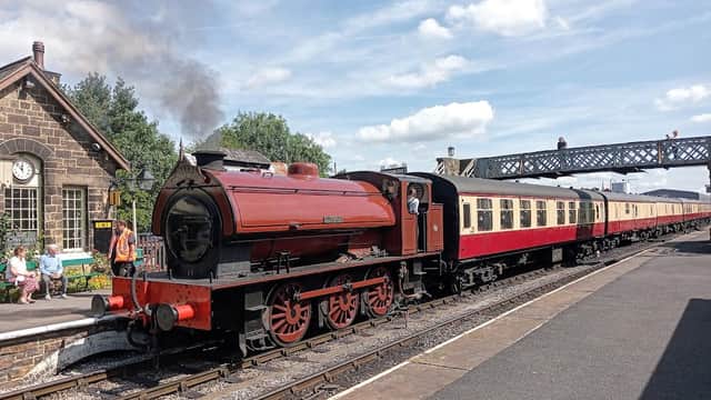 A vintage steam train at Embsay Station, with passengers on the platform and a historic building in the background.