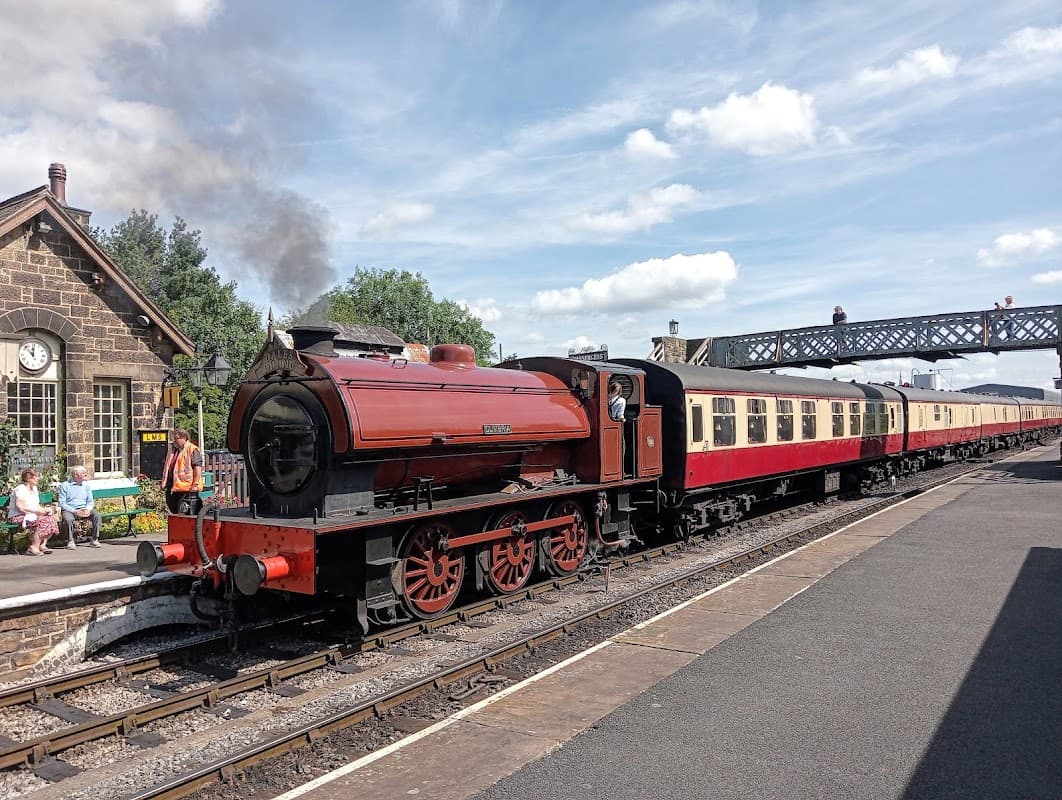 A vintage steam train at Embsay Station, with passengers on the platform and a historic building in the background.