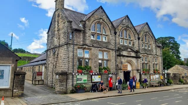 Historic stone building with arched windows, colorful flower boxes, and people entering, set against a blue sky.
