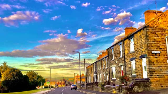 Burleigh Street West Commuter Car Park with stone houses, lush greenery, and a vibrant sky filled with clouds.
