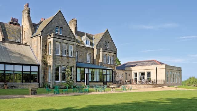 Victorian-style hotel with large windows, green lawn, and outdoor seating against a clear blue sky.