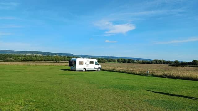 Expansive green field with a caravan parked under a clear blue sky, surrounded by rolling hills in Yorkshire.