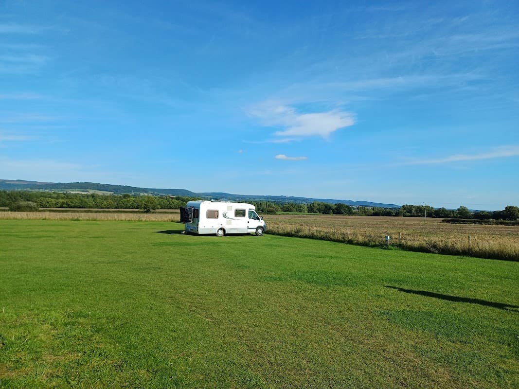 Expansive green field with a caravan parked under a clear blue sky, surrounded by rolling hills in Yorkshire.