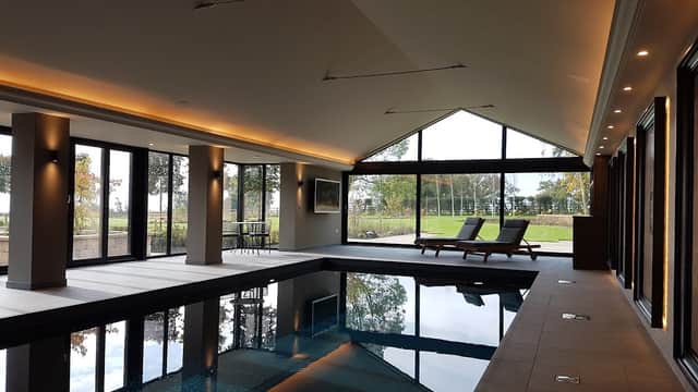 Modern indoor pool area with large windows, sleek lighting, and lounge chairs overlooking a scenic outdoor view.