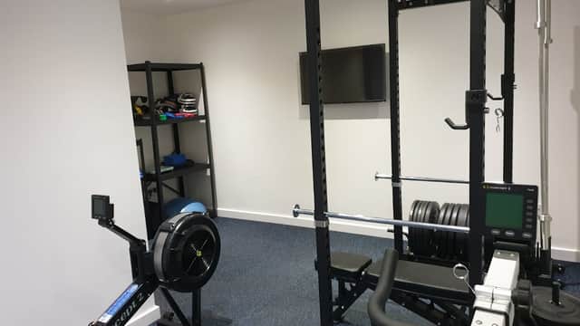 Fitness equipment including a rowing machine, weight rack, and exercise bench in a well-lit gym space.