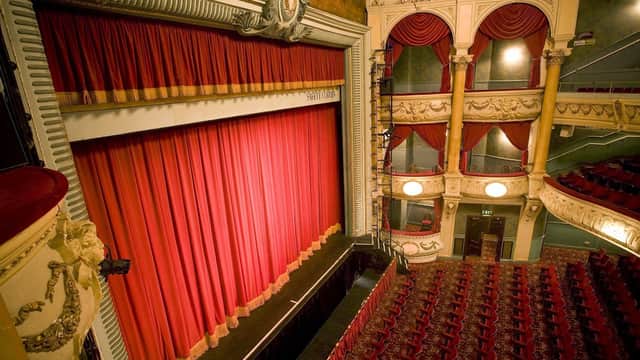 Ornate theater interior featuring a grand red curtain, plush seating, and decorative balconies in the Grand Opera House, York.