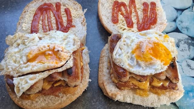 Two sandwiches with fried eggs, melted cheese, and sausage, topped with ketchup on a gray countertop.