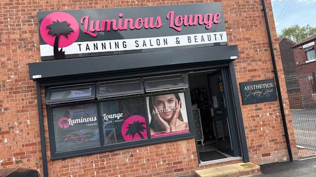 Luminous Lounge sign on a brick building, showcasing a tanning salon and beauty services with palm tree logo.
