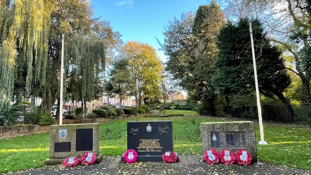 Memorial stones surrounded by trees and greenery, adorned with wreaths in a peaceful park setting.