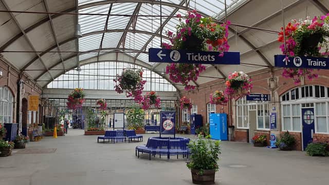 Brightly lit station interior with hanging flower baskets, ticket and train signs, and seating areas.
