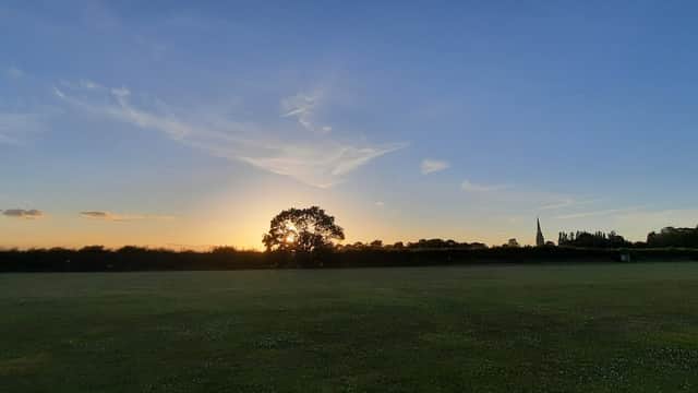 Sunset over a grassy field with a silhouette of a tree and a church spire in the distance.