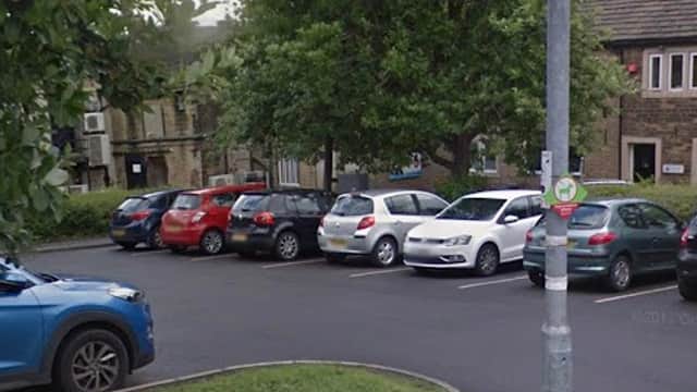 Car park with several parked cars, surrounded by greenery and buildings in Honley, Yorkshire.