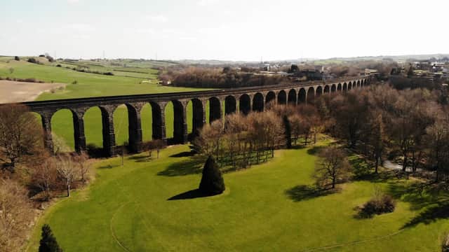 Aerial view of Watermeadows Park featuring a large stone viaduct and lush green fields under a clear sky.