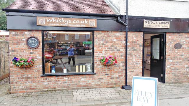 Brick exterior of Whiskys shop with flower boxes, signs for whisky and cards, and a sandwich board outside.