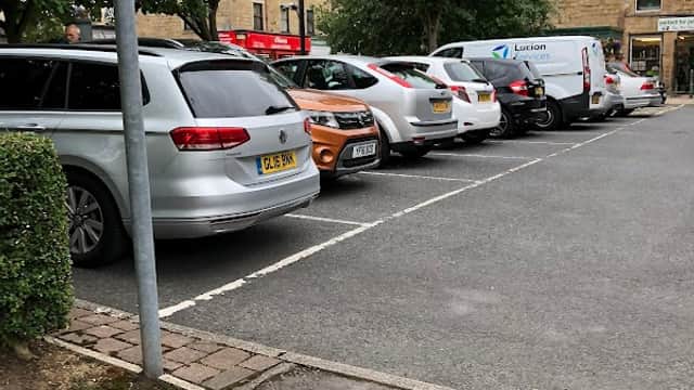 Car park with several parked vehicles, trees lining the sides, and a building in the background.