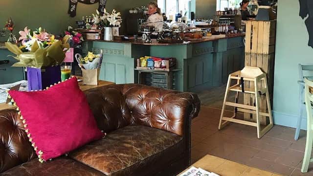 Cozy cafe interior with a leather sofa, wooden tables, flowers, and a bustling counter in a warm, inviting atmosphere.