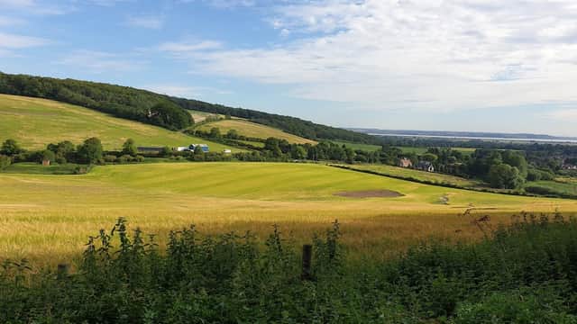 Lush green hills and fields under a blue sky, with a distant view of houses and trees in South Cave, Yorkshire.