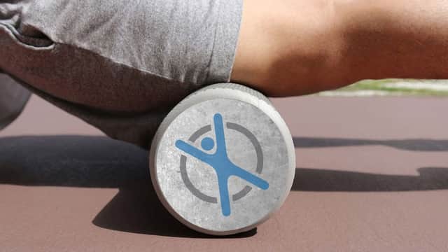 A person using a foam roller with a blue FLEX Pilates logo on a brown exercise mat.