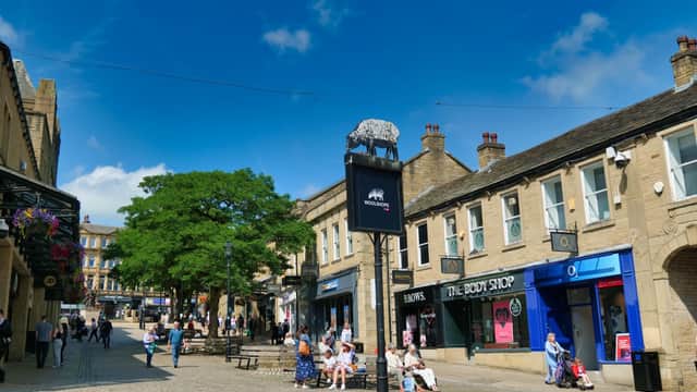 Woolshops shopping area in Halifax, featuring stone buildings, a vibrant tree, and shoppers enjoying a sunny day.