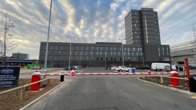 Entrance to JustPark car park with barrier, modern building in background, and dramatic cloud-filled sky.