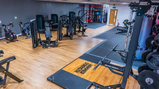 Modern gym interior featuring various weightlifting machines, exercise bikes, and free weights on wooden flooring.