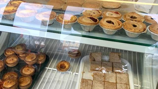 Display case filled with various baked goods, including pastries, pies, and squares, in a bakery setting.