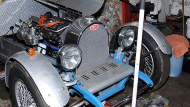 Classic car with exposed engine and chrome details, parked inside a garage with tools and equipment nearby.