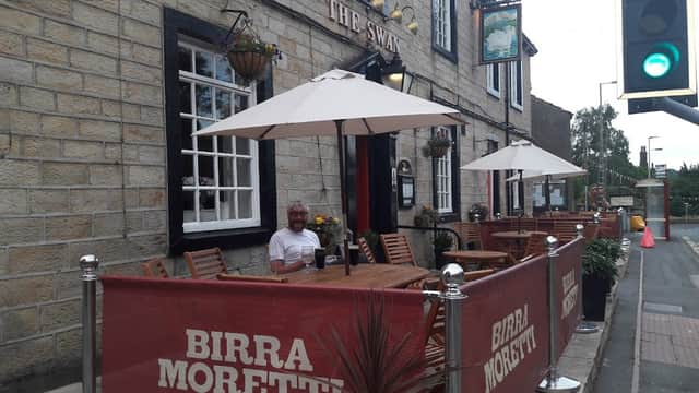 Quaint pub with outdoor seating, umbrellas, and a "Birra Moretti" banner, set in a stone building in Addingham.