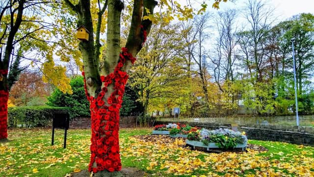 A tree adorned with red poppies, surrounded by autumn leaves and flower beds in Sparrow Park, Birkenshaw.