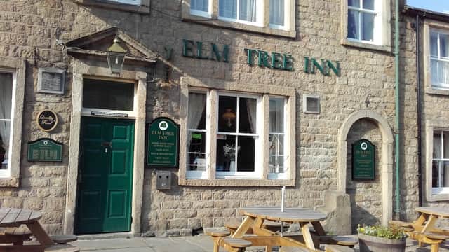 Stone facade of Elm Tree Inn with green door, windows, and wooden benches outside in Embsay, Yorkshire.