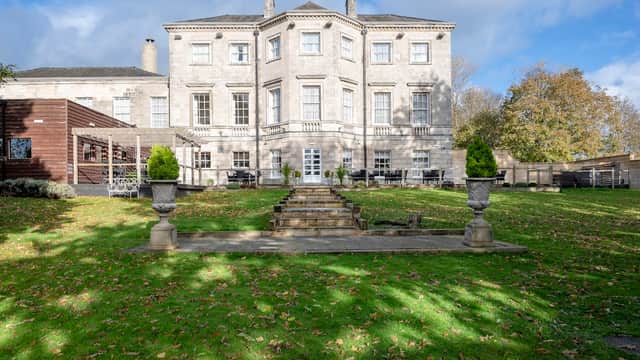 Aston Hall Hotel features a grand stone facade, manicured lawns, and decorative planters under a blue sky.