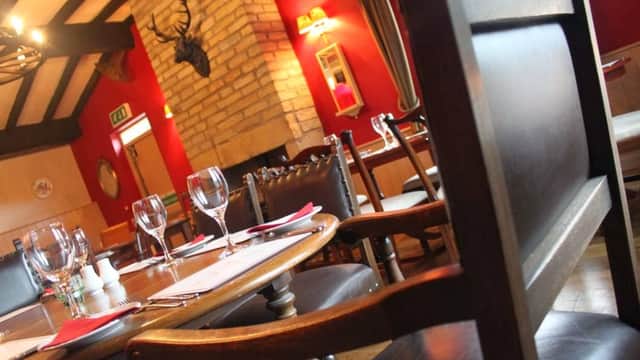 Cozy bar interior with wooden chairs, a stone fireplace, and red walls, featuring a mounted deer head and dining setup.