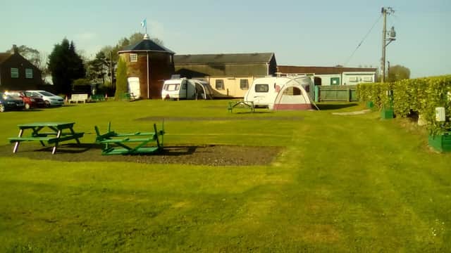 Millhouse Caravan Site features green grass, picnic benches, caravans, and a building in a rural setting.