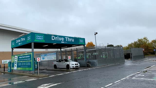 Drive-thru sign at Monks Cross North shopping center, with a gray car parked in front under a cloudy sky.