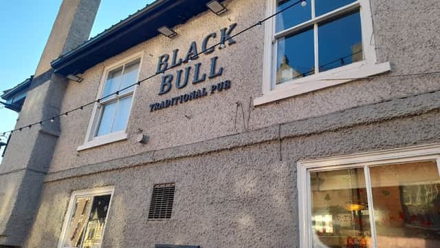 Exterior of the Black Bull pub in Thirsk, featuring a sign and large windows under a clear blue sky.