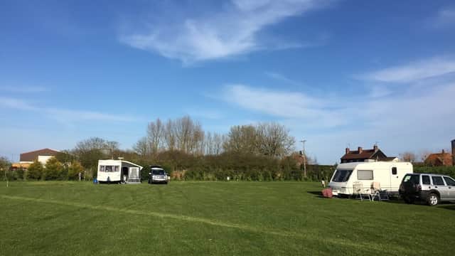Caravans parked on green grass with trees in the background under a clear blue sky at Rectory Farm CL Caravan Site.