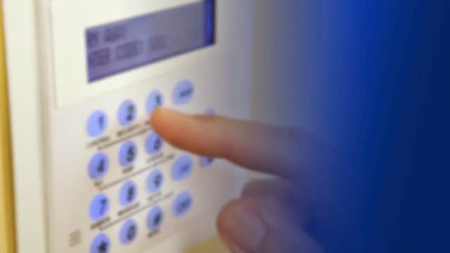 A hand pressing buttons on a security system keypad with a digital display.