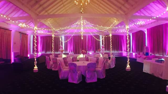 Elegant event space with round tables, white chair covers, and purple lighting, adorned with string lights and chandeliers.