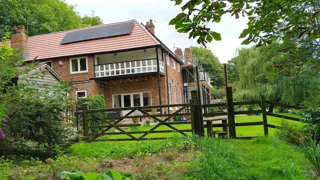 A charming brick house with solar panels, surrounded by greenery and a wooden fence in Over Dinsdale, Yorkshire.