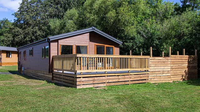 Wooden lodge with a deck, surrounded by greenery and trees, set in a grassy area at Kiplin Lodge Park.
