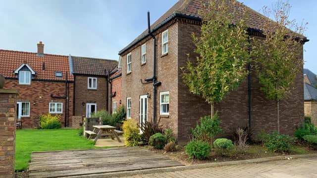 Two-story brown brick building with a garden, picnic table, and greenery in a residential area of Filey, Yorkshire.