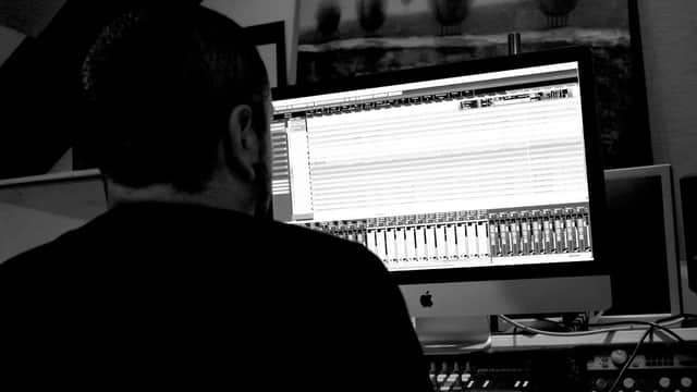 A person working on a music production setup with a large computer screen displaying audio tracks.