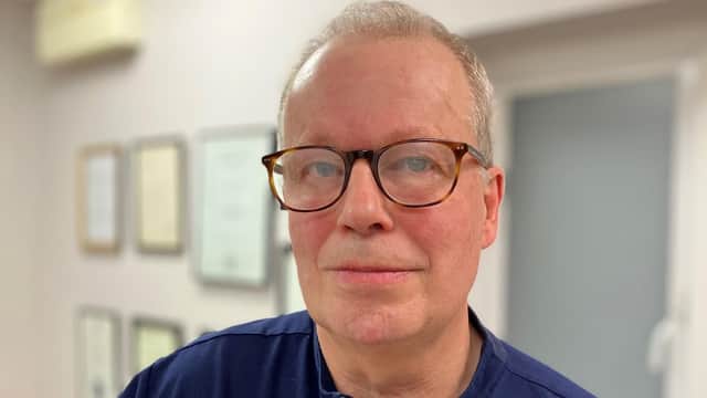 Dr. Paul Charlson wearing glasses, in a clinic setting with framed certificates in the background.