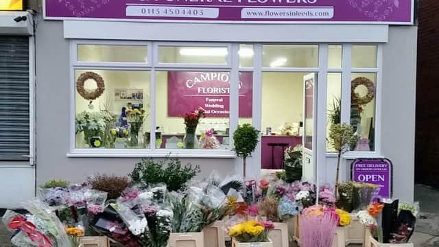 Colorful flower arrangements displayed outside Campions Florist, with a sign indicating open hours and services offered.