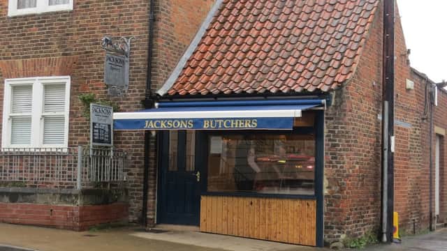 Shopfront with a blue awning reading "JACKSONS BUTCHERS," brick walls, and a sign hanging above.