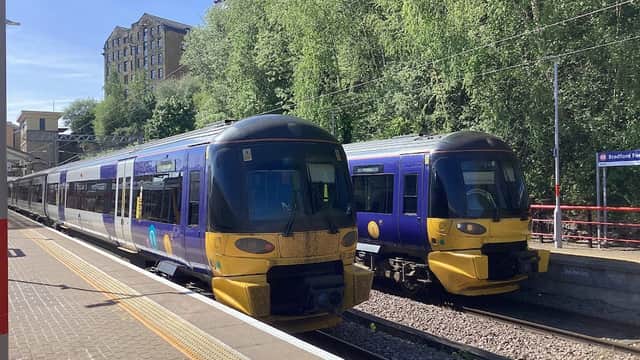 Two trains at Bradford Forster Square station, surrounded by greenery and a clear blue sky.