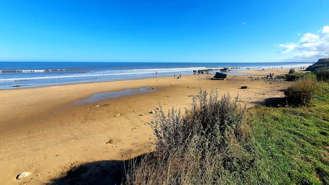 Wide sandy beach at Fraisthorpe with gentle waves, blue sky, and sparse vegetation along the shore.