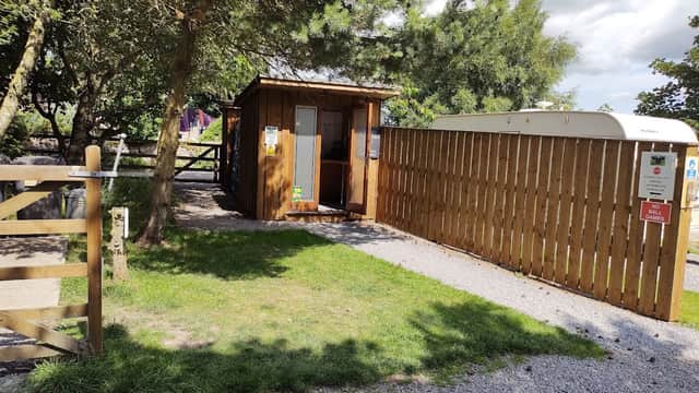 Wooden reception cabin with a fenced area, gravel path, and greenery at Cow Close Caravan & Camping in Bellerby, Yorkshire.